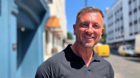 A man, Jason Burrill, stood on a pavement by a street.