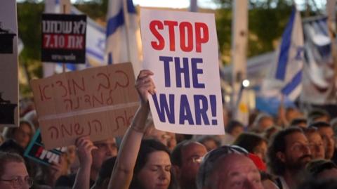 Protesters march holding aloft signs, one reads 'Stop the war!'