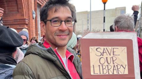 Tony Vaughan stands with campaigners outside the library at a protest before he became an MP and holds a placard saying "save our library".