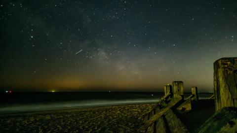 night sky image from a beach overlooking the sea. Lots of bright white spots in the sky and one streak of light showing a meteor streak