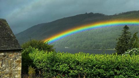 A colourful rainbow over a loch, with dark clouds looming in the background.