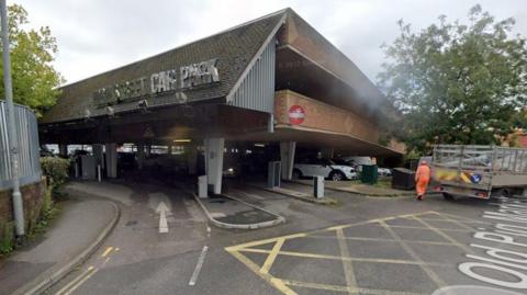 A multi-story car park in Taunton. There are cars parked on the bottom floor of the building, with a waste truck exiting.
