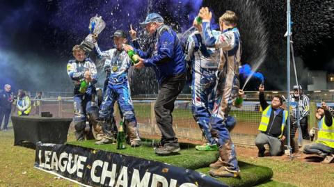 Champagne sprays in the air with riders in blue and white celebrating