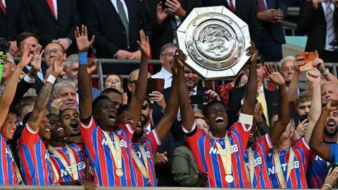 Marc Guehi lifting the Community Shield trophy with Crystal Palace players celebrating around him.