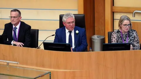Three people sitting in the Holyrood chamber