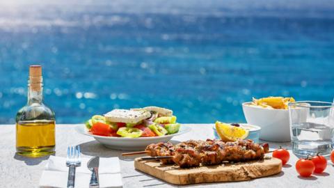 A table of Greek food with the sea in the background