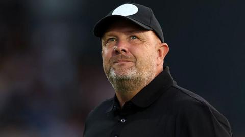 Andy Woodman is wearing a dark shirt and a black baseball hat with a white spot.