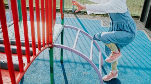 A child plays on a colourful climbing frame on a sunny day. The child's face is not visible.