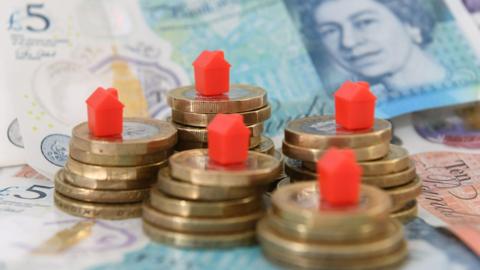 Stock image of red models houses on a pile of coins and bank notes.