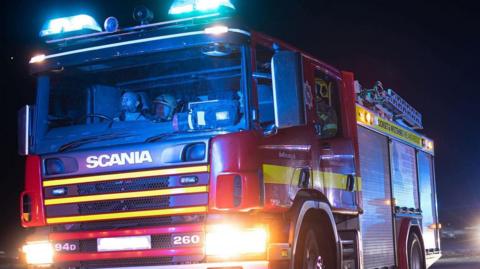 A Dorset and Wiltshire Fire Service fire engine driving in the dark with blue lights flashing
