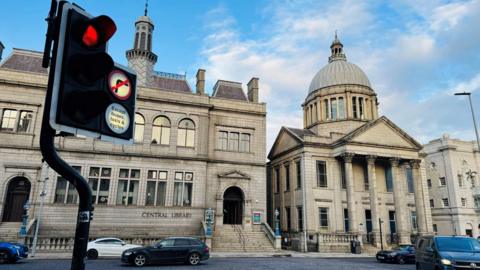 Traffic lights on red with a no right turn sign, cars and buildings in the background.