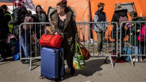 A woman stands with bags and suitcases as refugees from Ukraine wait for the bus after they crossed Ukrainian-Polish border at the border crossing in Medyka, southeastern Poland on April 8, 2022