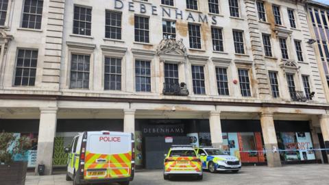 A police cordon around the former Debenhams store in Nottingham. Two police cars and a police van are parked outside the building and police tape can be seen in the background