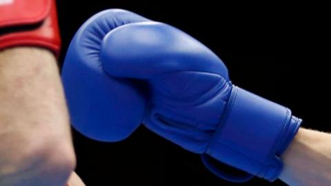 A boxer's hand in a blue boxing glove is fended away by another boxer's hand in a red boxing glove