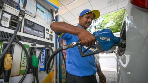 An attendant at a petrol station is pictured filling a car with diesel in India.