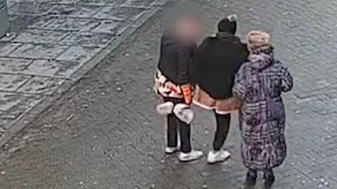 A CCTV image of three people on a street. They are wearing winter coats.
