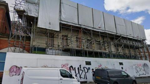 The pub has scaffolding, whit boards with graffiti surrounding it 