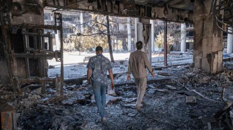  Two unidentified security men walk through the debris of the headquarters of the Islamic Republic of Iran News Network, which was destroyed in Israeli strkes