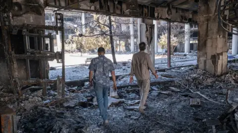  Two unidentified security men walk through the debris of the headquarters of the Islamic Republic of Iran News Network, which was destroyed in Israeli strkes