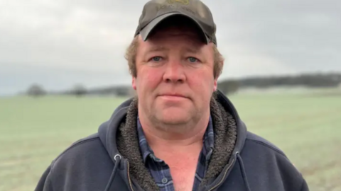 A man wearing a cap stood in a field looking at the camera