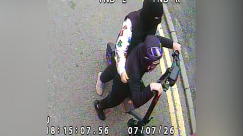 CCTV image of two people on an electric scooter. They have their heads and faces covered and are wearing mostly black clothing