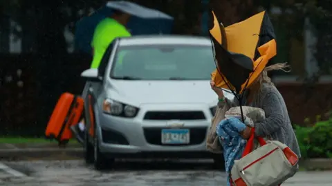 A woman holds an umbrella while arriving at a shelter as Hurricane Milton approaches