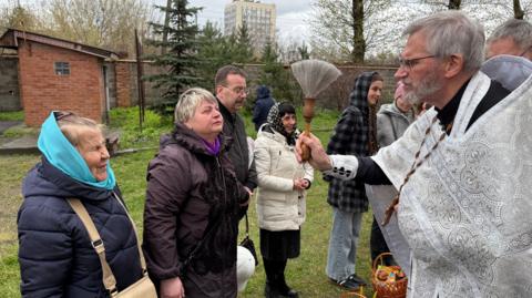 Priest dressed in a white robe giving his blessing to churchgoers.