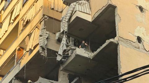 A view from below shows a man walking on the floor of a destroyed balcony after an Israeli military strike targeted a residential apartment block in southern Beirut. 