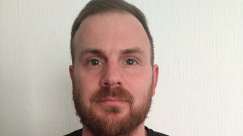 A headshot of Tony Pascall. He is standing in front of a white wall and looking directly into the camera.