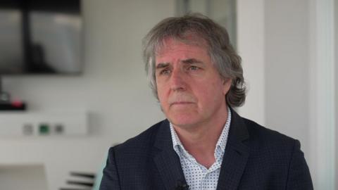 Steve Rotheram, who has grey hair and wears a dark suit, speaks to the camera