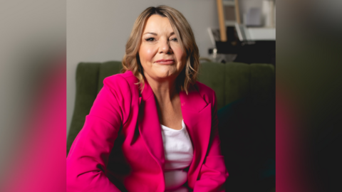 Woman in bright pink blazer and white t shirt poses for professional photograph.