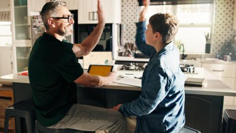 A father and son high five each other while sitting a desk and revising for an exam together