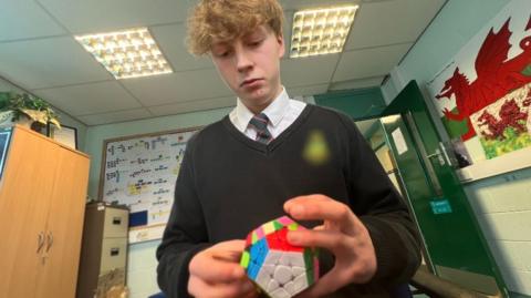 Aidan playing with a Rubik's cube while he sits in a school classroom.