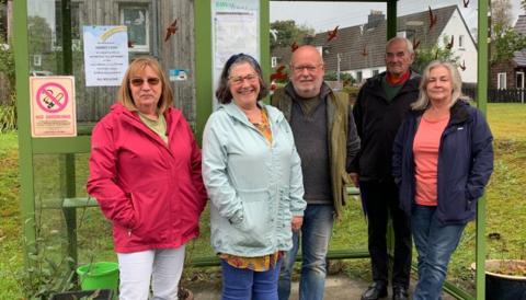 A group of five people - three men and two women - standing in a bus shelter in Glentrool. 