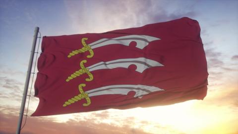 The red flag with three seax swords printed on it, with the sun rising or setting behind it creating a partial silhouette.