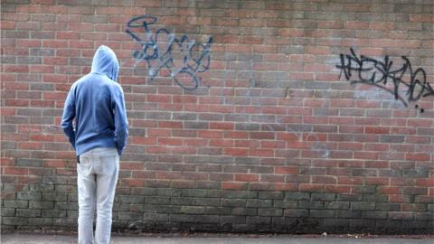 teenager in hoodie standing by graffitied wall