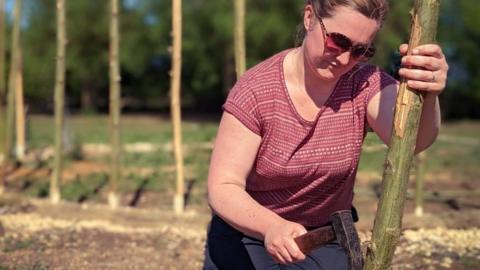 A volunteer works wood using traditional tools