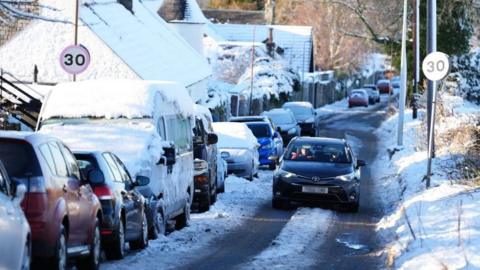 A wintry scene of cars is shown on a street in snowy Scotland.