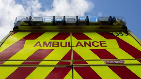 The rear of an ambulance with red and fluorescent yellow chevrons and blue lights on the roof.
