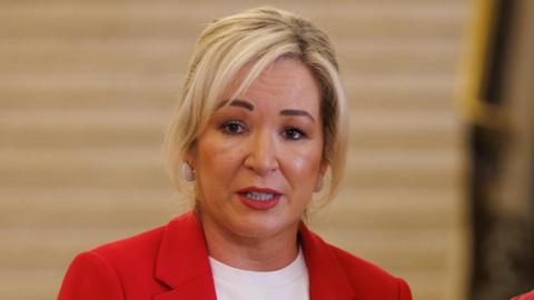 Michelle ONeilll has blonde hair, a red jacket and white tshirt 