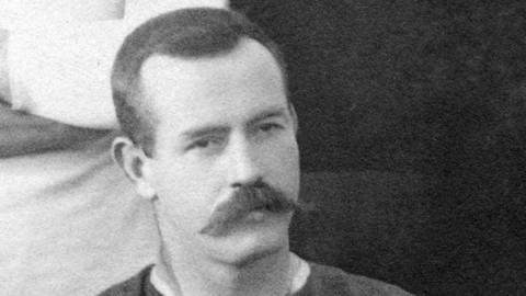 A black and white picture of Dave Gallaher. He has short dark hair and a large thick moustache. 