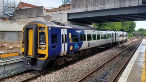 A Northern Train with two carriages on the tracks parked at a rail station.