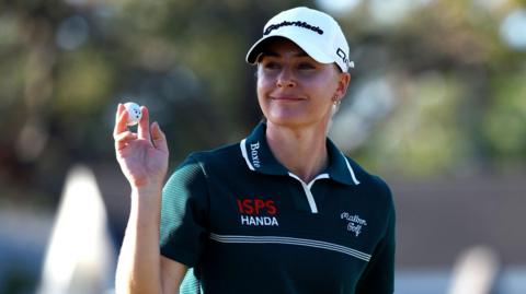 English golfer Charley Hull holds up the ball after making a putt during the third round of The Annika