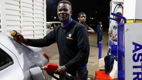 A pump attendant, in a black sweater written Astrol fuels a car at an petrol station in Kenya