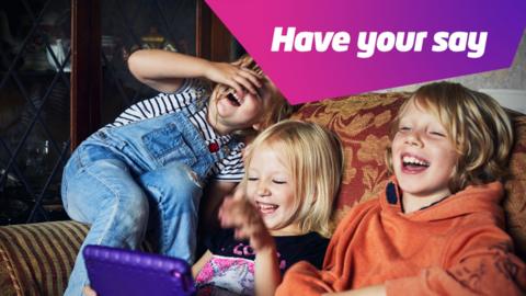 three children sat together on a sofa sharing a tablet laughing with one another