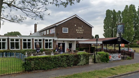 Street view of the Rocket Pool pub. It is next to a small green play area with green slides.