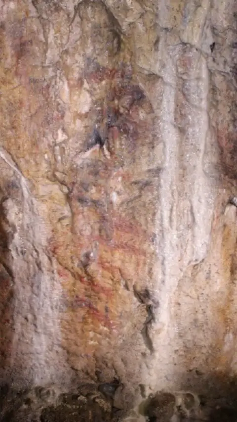 A dark red area of ancient cave art on light rock