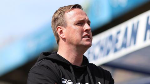 Wycombe boss Mike Dodds standing in front of a dugout