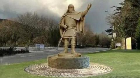 A illustration of the Viking statue, set on a plinth with a circle of paving surrounding the base. It is on a grassed area with a road junction in the background.