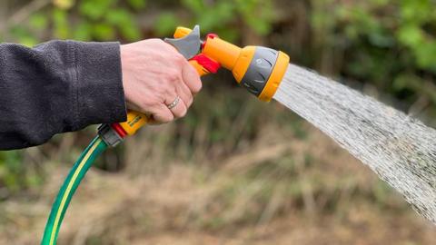 Close up of a hand holding a hosepipe gun with a shower of water coming out of the nozzle
